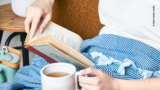 Frau auf Sofa mit Buch und Tee