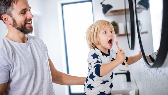 Vater und Kind beim Zähneputzen vor Spiegel
