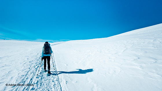 Warm gekleidete Person wandert mti Stöcken durch den Schnee