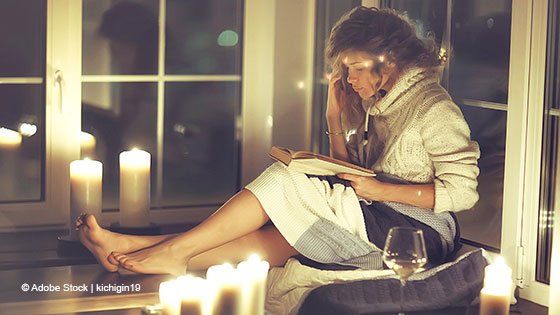 Frau sitzt gemütlich mit einem Buch bei Kerzenschein und liest