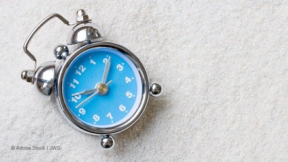 blauer wecker auf weissem sand