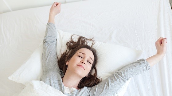Frau streckt sich im Bett.
