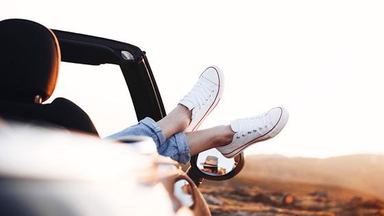 Frau streckt Sneaker aus dem Autofenster.