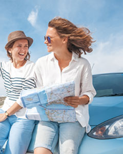 Zwei Frauen sitzen mit Straßenkarte auf der Motorhaube